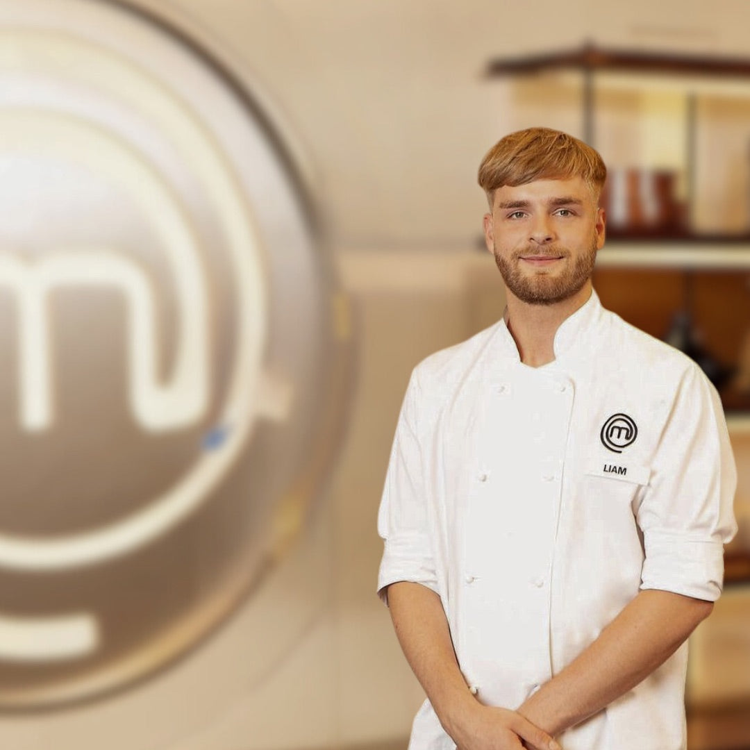 Person in a white chef's jacket with a MasterChef logo, standing in a kitchen setting.